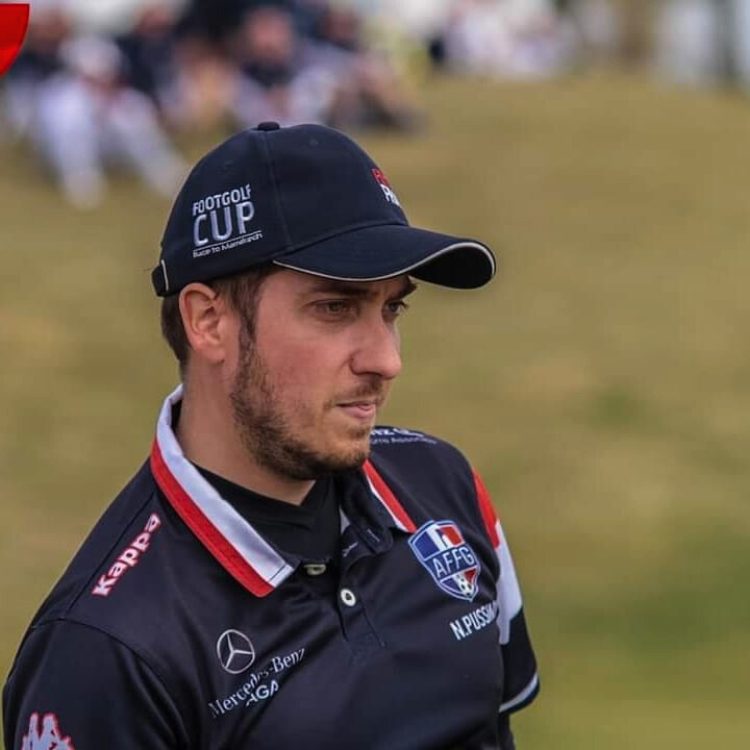 Homme en polo noir avec logos Mercedes, Kappa, AFFG, casquette FootGolf Cup sur terrain herbeux.